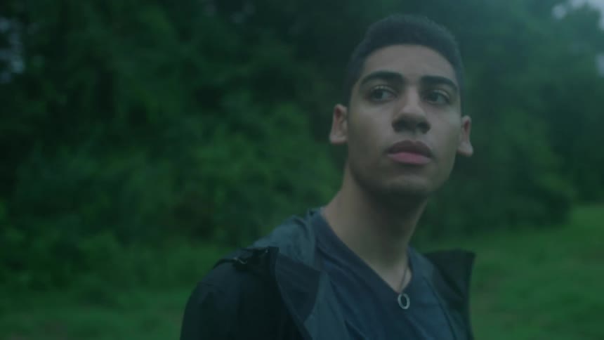 A young men wearing a black coat standing in a foggy drizzly greenfield