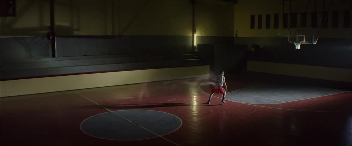 Person plays basketball alone in a dim gym with flashing lights