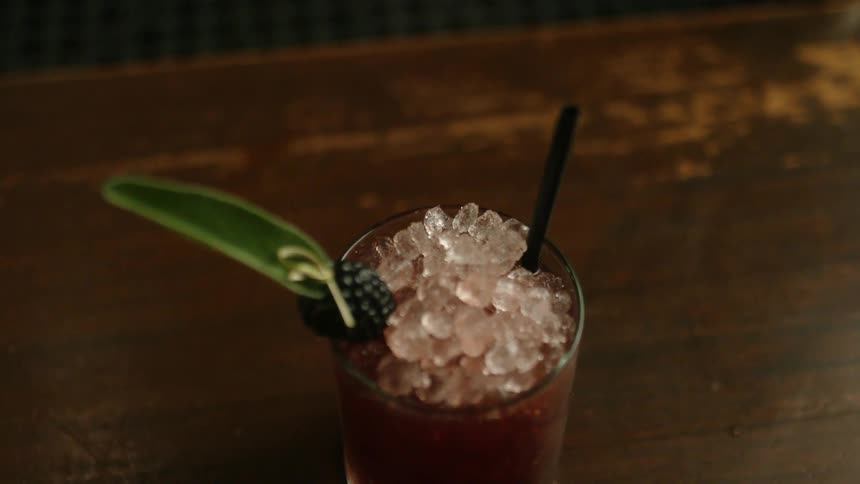A bartender sticks a straw in a cocktail overflowing with ice