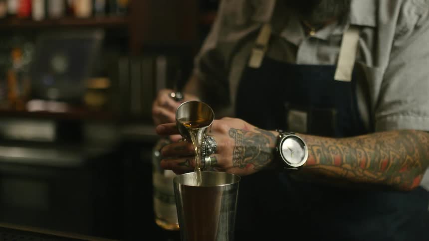 A bartender pours alcohol into a jigger and then into a mixing tin