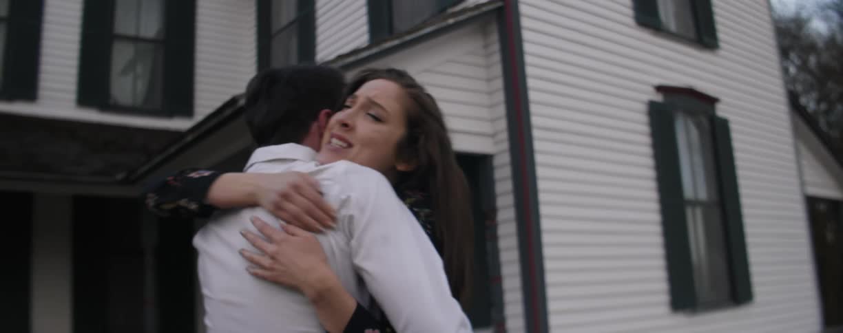 A man and woman embrace and hug each other outside a house during the day