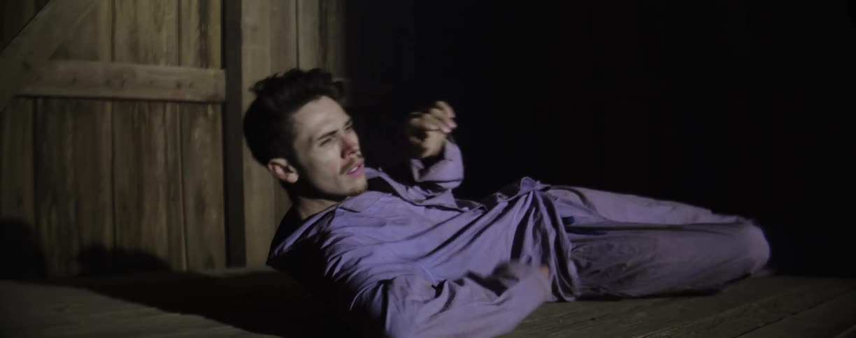 A man awakens on the floor in a barn as a door is opened