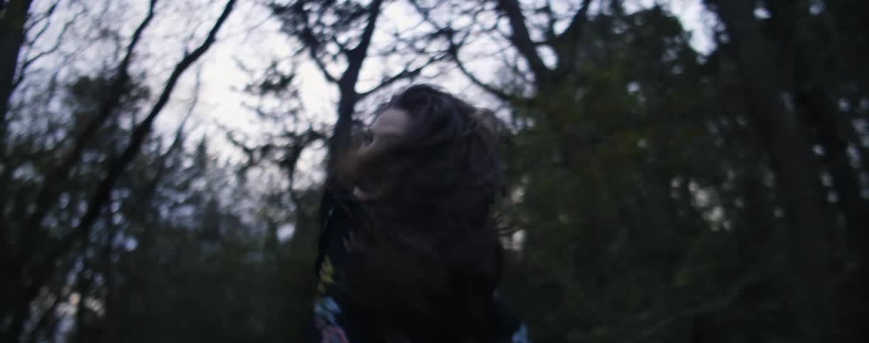 A woman twirls and laughs as she runs in a natural setting