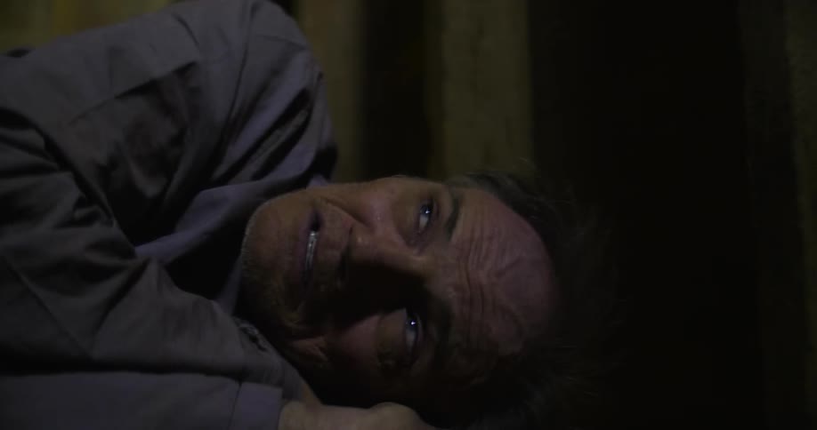 A man on the floor grimaces before closing his eyes