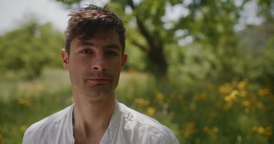Man poses standing in meadow with yellow flowers