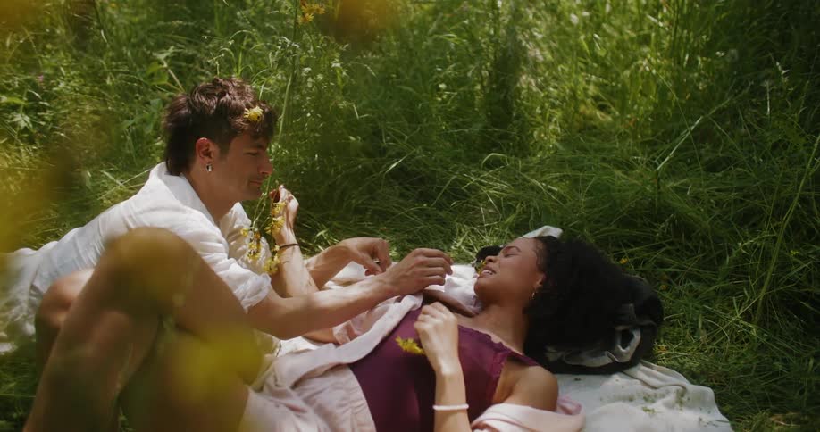 Couple in love lying on the grass with wreath of yellow flowers on their heads