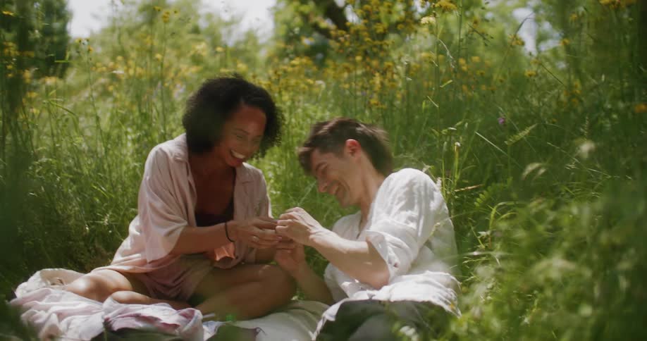 Man and woman sitting and laying in the grass on a blanket laughing and smiling on a bright sunny day