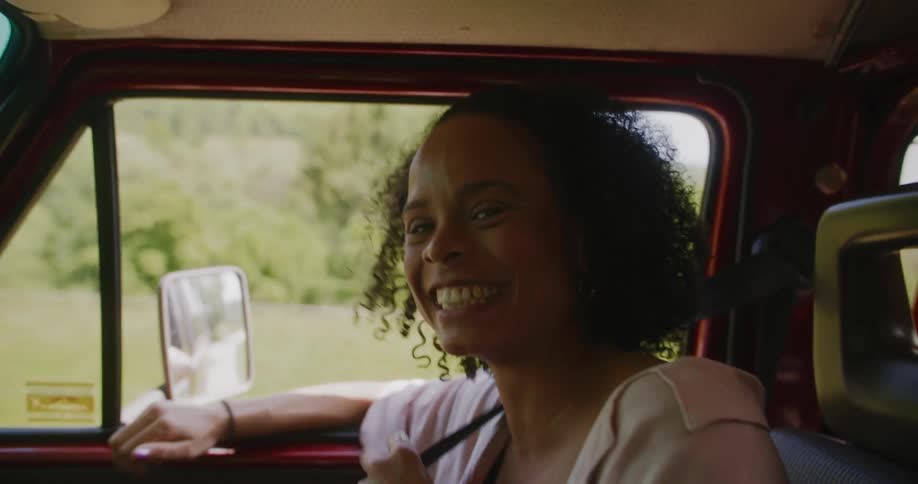 A close up of a young woman in the passenger seat of a car wearing her seatbelt while laughing and smiling