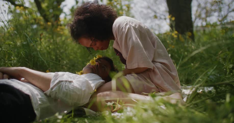 Man laying on a womans lap sitting on a blanket in the middle of a grassland while kissing each other