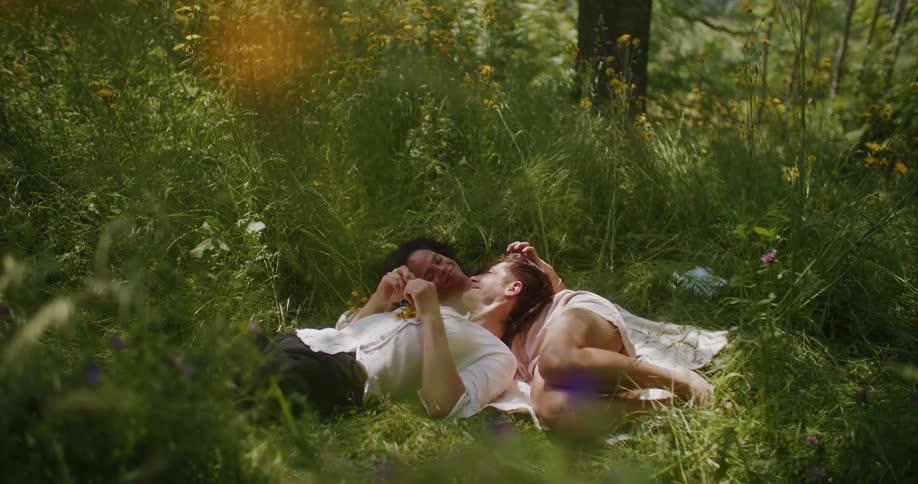 Couple in love lying on the grass with wreath of yellow flowers on their heads in the middle of the forest