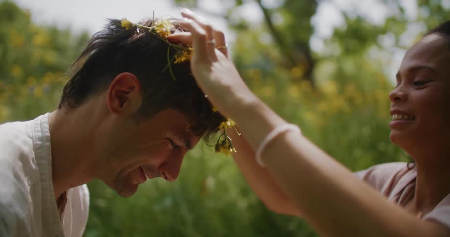 A woman putting a flower band around a mans head in front of her as he smiles and looks at her