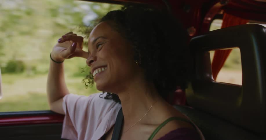 Close up of a young woman smiling in the front seat of a car laughing while the car is driving in nature