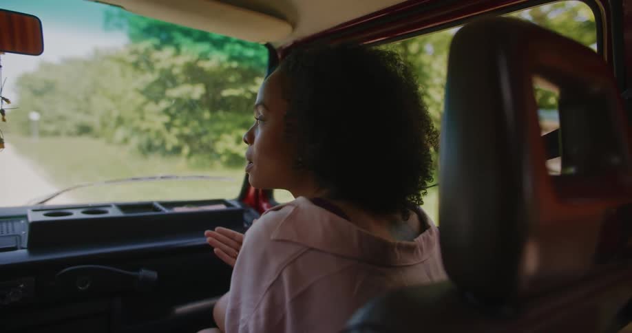 Young woman sitting in the passenger seat of a car while talking to someone in the driver seat as the car is parked
