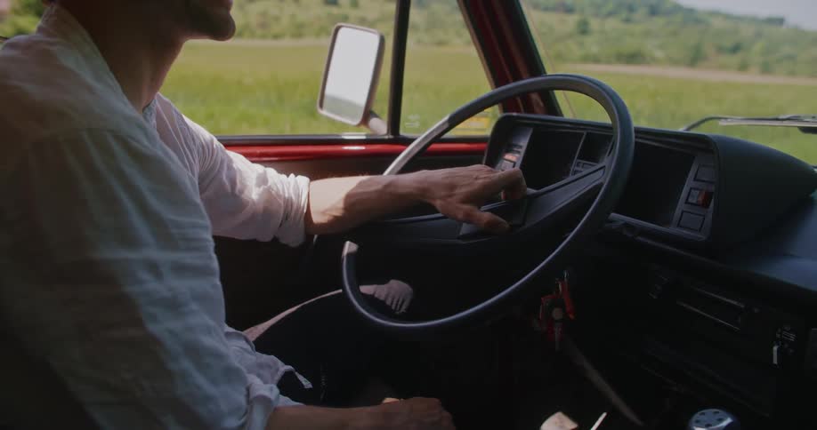 Man sitting in the front seat of a car with his hand on the steering wheel while talking to someone