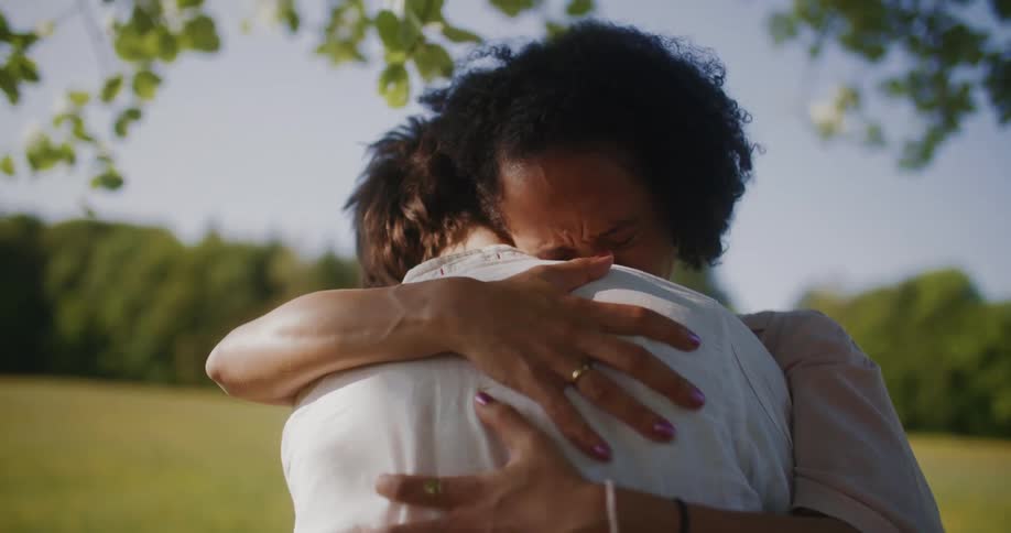 Two people hug tightly outdoors under tree near field