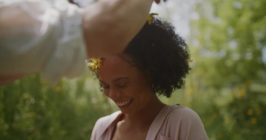 Woman preens with a smile after male friend places flower crown on her head in field