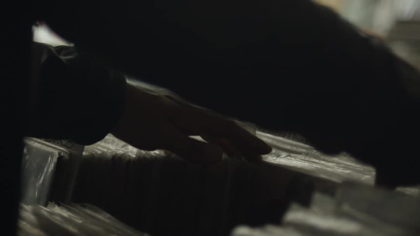 Close up of a persons hands rummaging through records wrapped in plastic stacked together