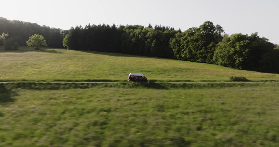 Colorful caravan drives along highway passing intersection and fields bordering woods