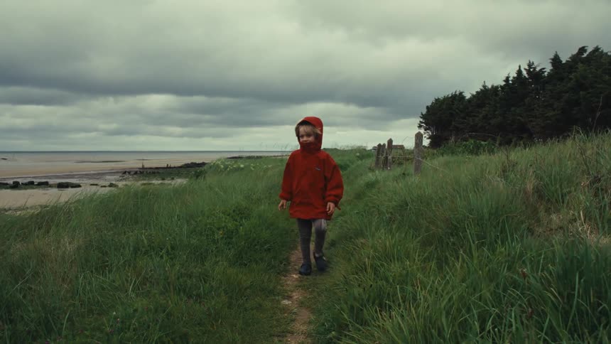 Toddler child walking on a path near the sea next to the beach on a cloudy day