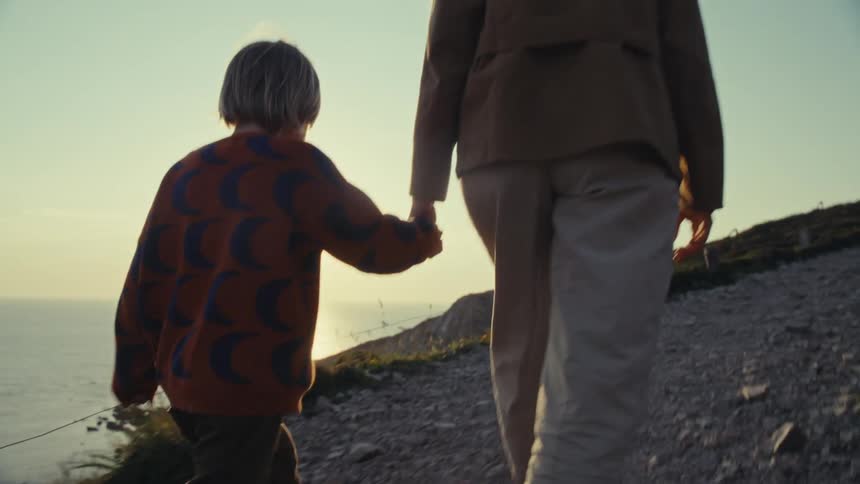 Woman and child walk up a trail holding hands during sunset