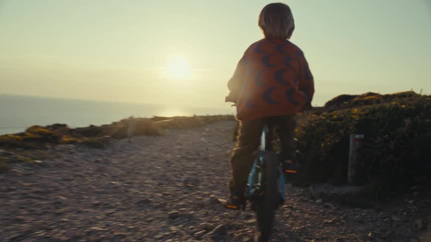 Child rides a bike on a rocky path by the ocean