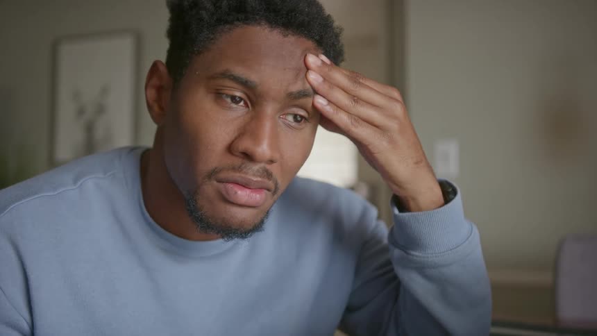 A man is sitting at his computer desk and thinking