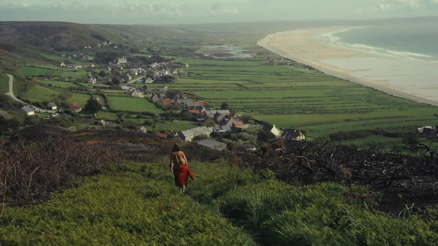 Mother and child walk down the hill towards the town next to a beach