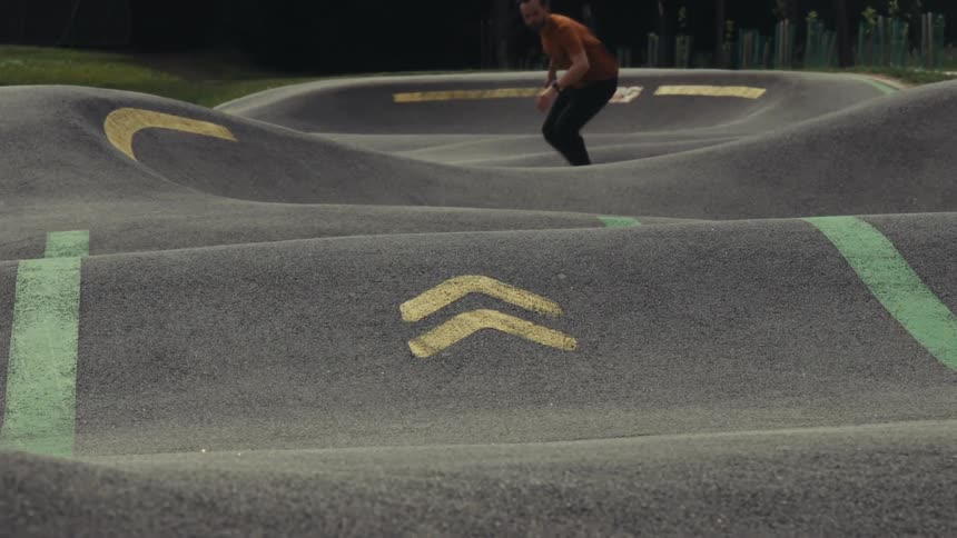 Skateboarder skating across bowls in a pump track skatepark