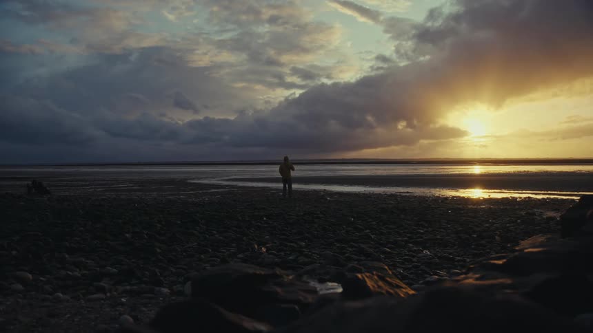 Person walks toward the water and stops to observe the sunset