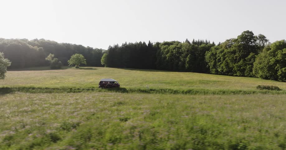 Van driving across a road through a field in forested surroundings in the countryside