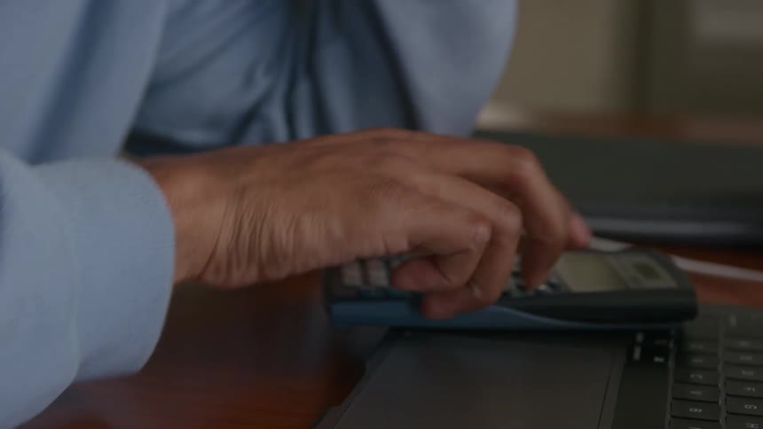 An extreme close up of a man writing on a notebook then grabbing a calculator and typing on it