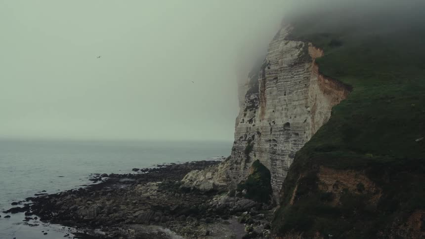 Birds fly around the cloudy cliffs on the shore of Normandy