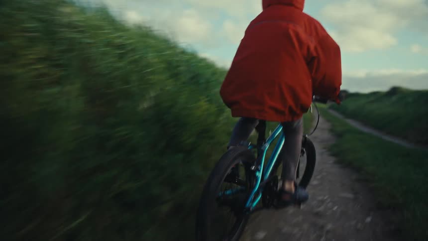 Young child riding a bicycle on a dirt road surrounded by tall grass