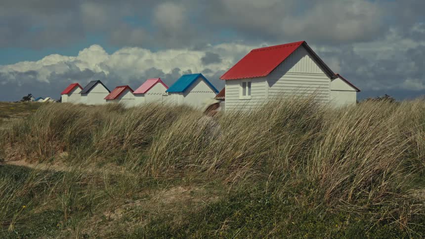 A small child runs through the tall grass in front of colourful beach houses