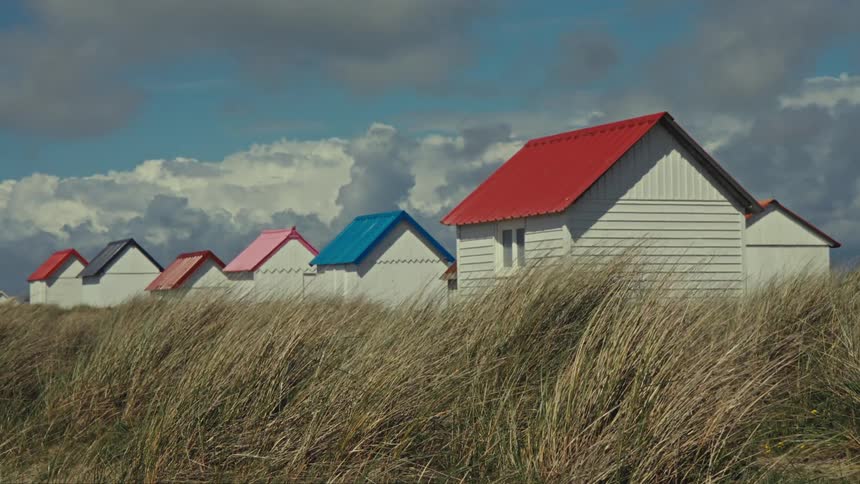 In an open field on a windy day there are several small houses with colorful roofs including shades of red and blue the absence of fences gives the area an open and inviting feel the houses are surrounded by lush green grass