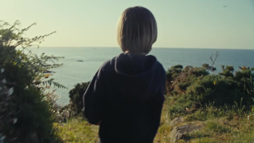 A child is walking on a trail next to the sea