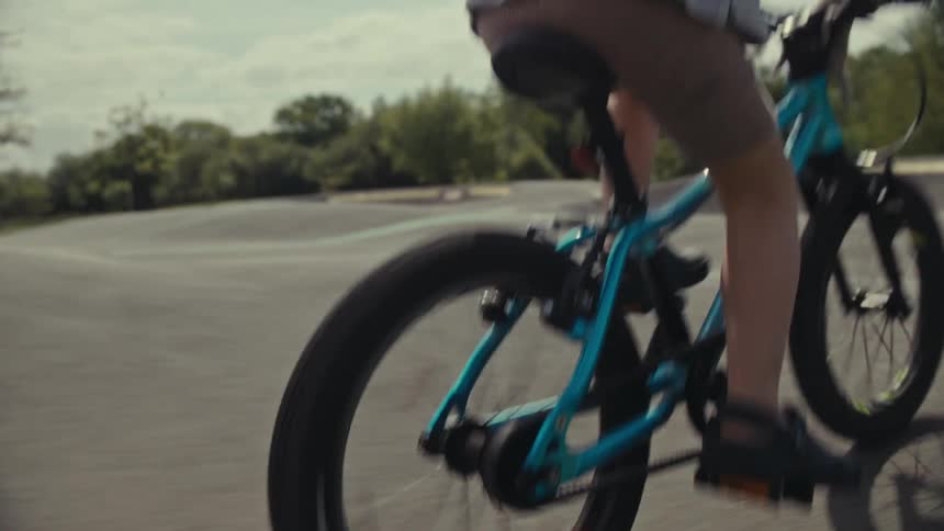 Young child rides a bicycle pump track course near woods on cloudy day