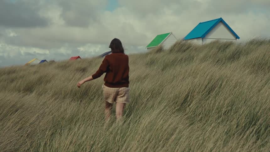 A woman walks through tall grass on a windy day