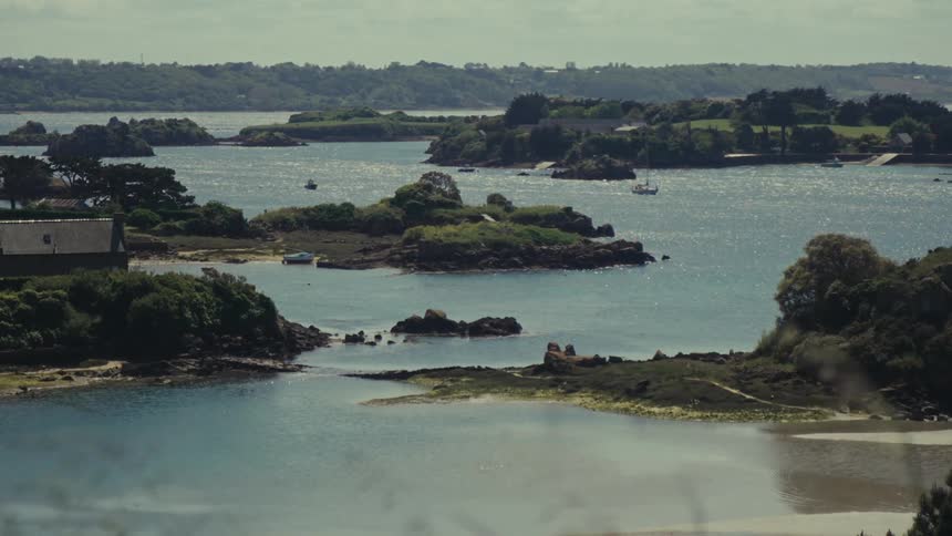 View of the French shoreline with a house and small islands with a boat in the distance