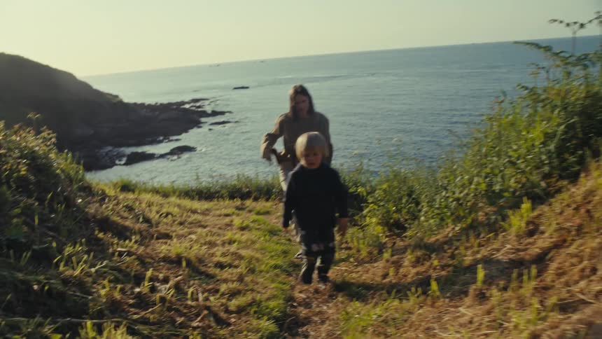 A woman and young child hike up the trail next to the sea