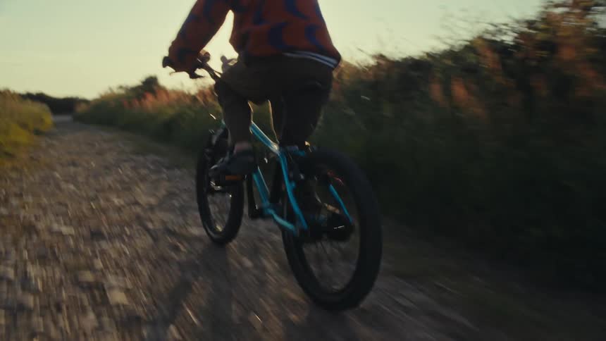 Young child riding a bicycle on a gravel road surrounded with tall grass