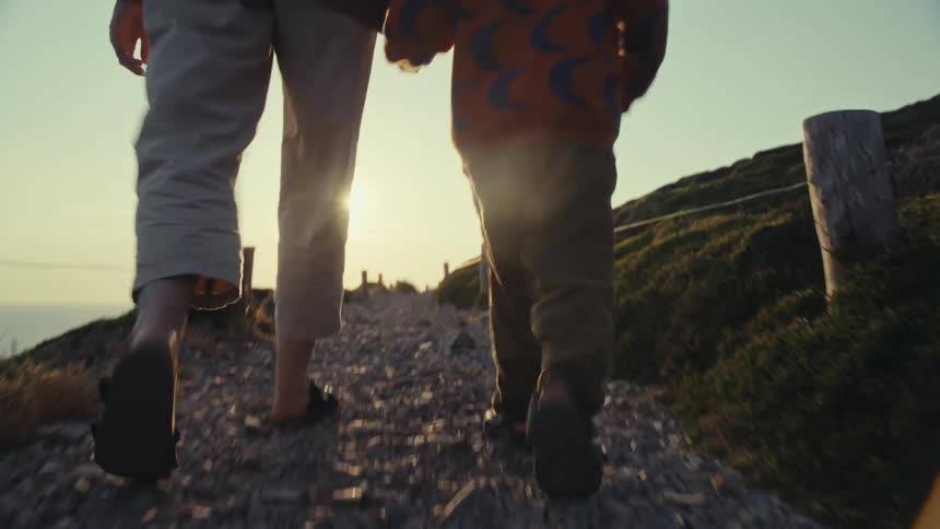 Young child hiking on a trail holding mother's hand next to the sea