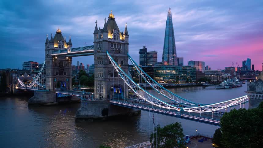 Traffic travels across a large bridge spanning a waterway in a metropolis as the sun sets