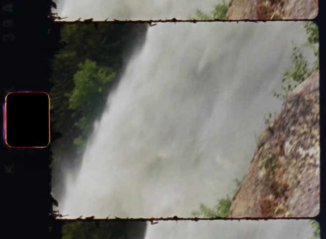 A tall powerful waterfall is filmed in motion from its top to the bottom of the falls with lush green vegetation surrounding it