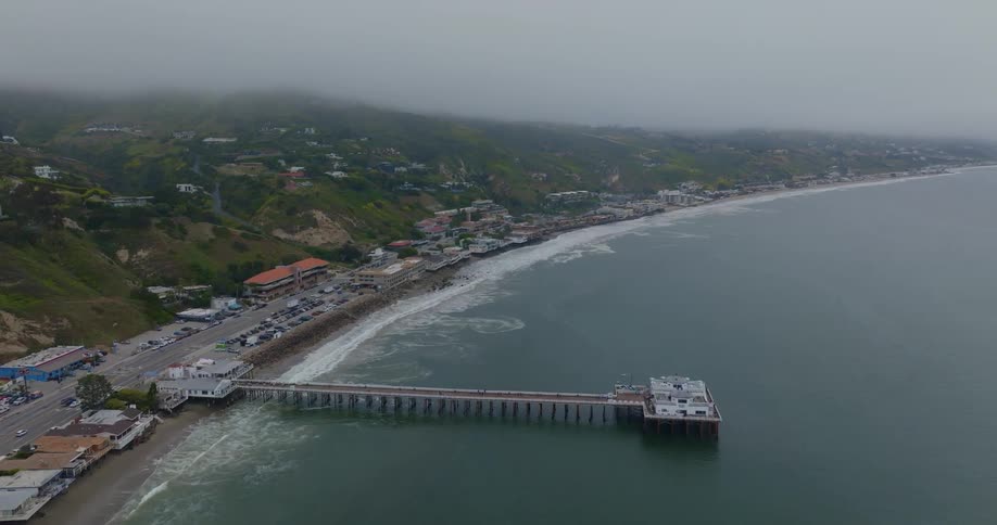 A foggy aerial shot of Malibu pier and PCH coastline stretching into the distance