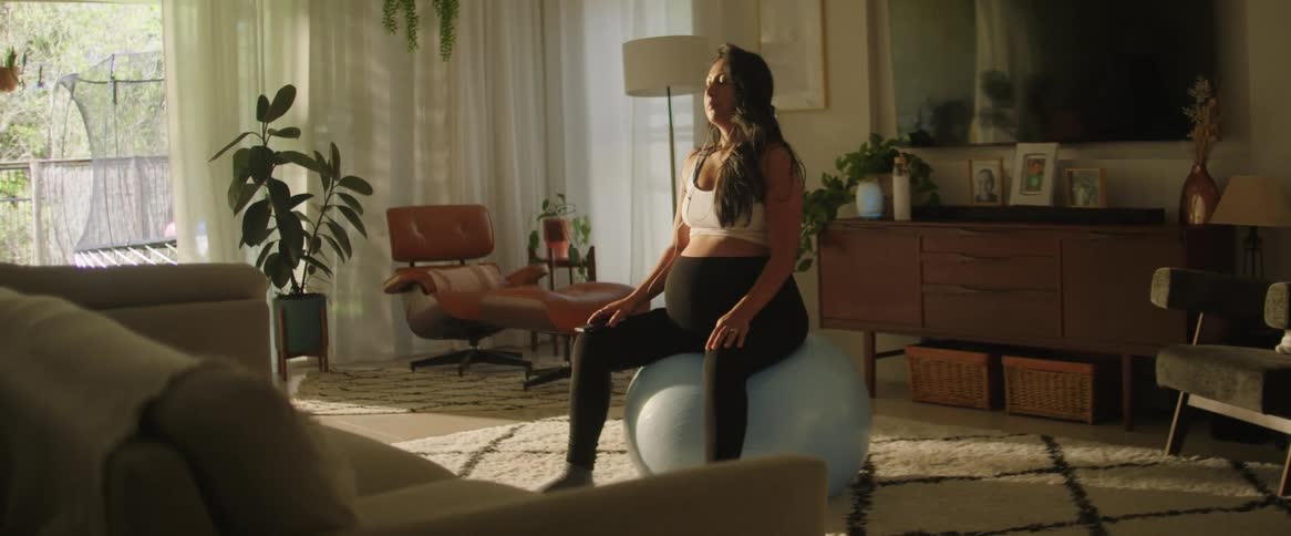 Pregnant woman indoors checking her phone before doing yoga sitting on a pilates ball