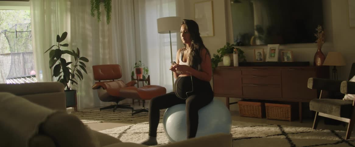 A woman puts in her earbuds on the yoga ball