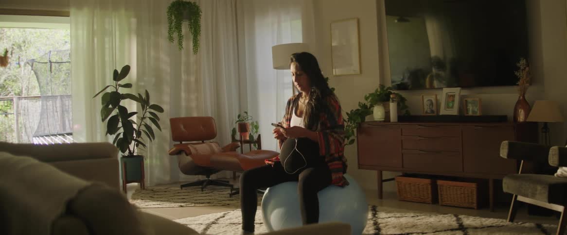 Pregnant woman sitting on a pilates ball listening to music on her smartphone