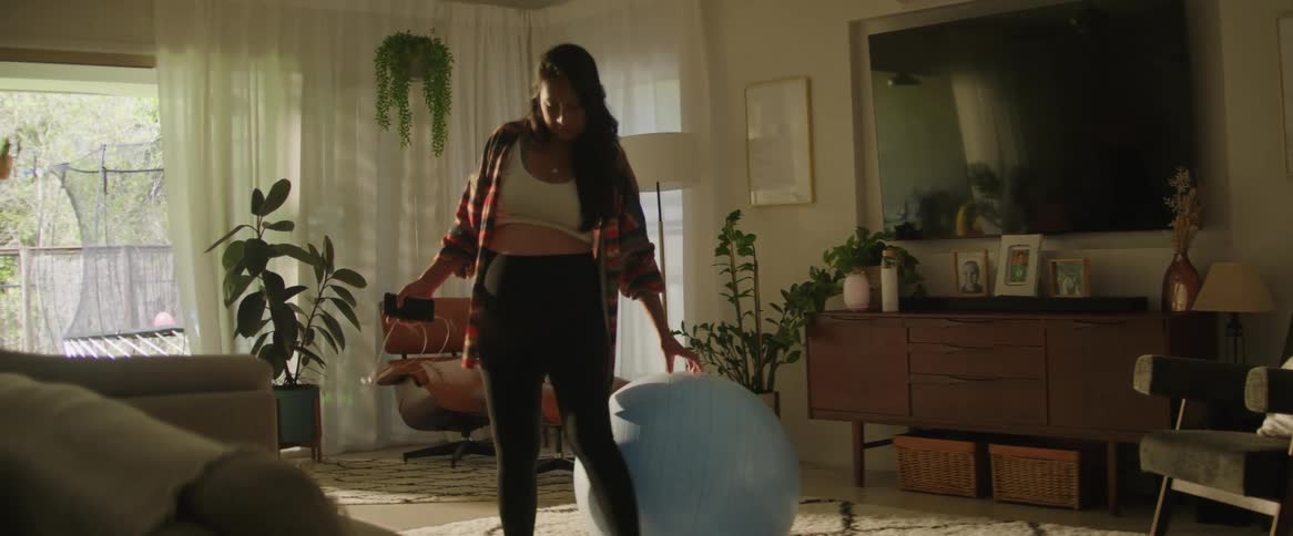 A pregnant woman finds solace in the middle of a room sitting on a yoga ball to relax