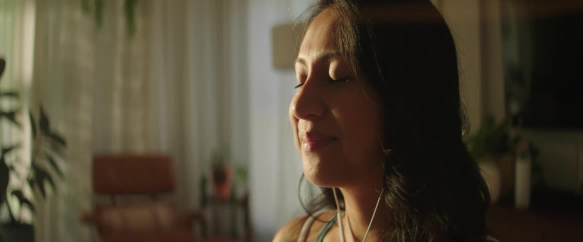 A pregnant woman rubs her stomach while sitting with her eyes closed indoors during the day